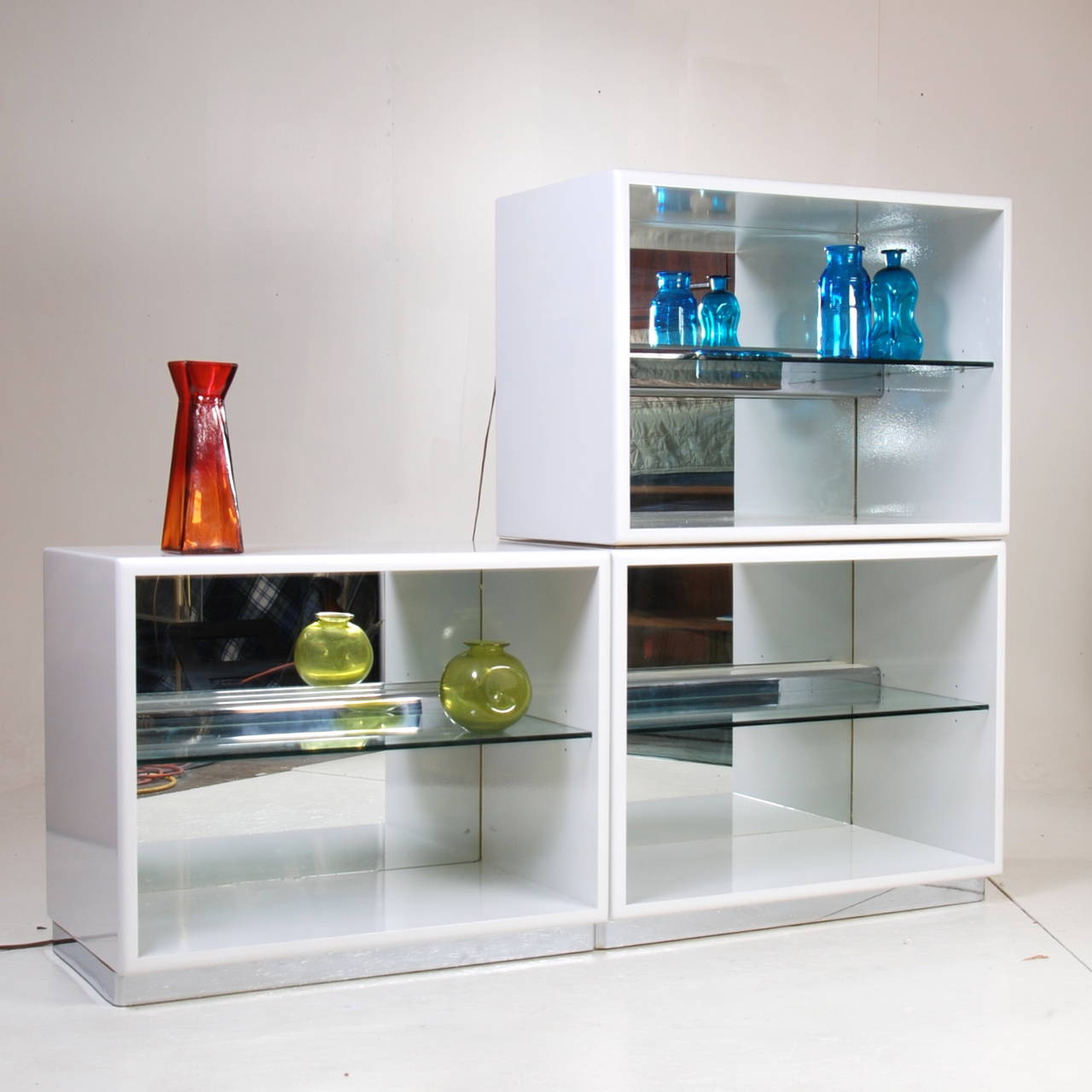 Amazing white lacquered and mirrored cabinets by Milo Baughman for Thayer Coggin. They sit on a chrome and wood base. They feature an interior light fixture behind a chrome bar, and an adjustable glass shelf.  Can be used side by side as a sideboard