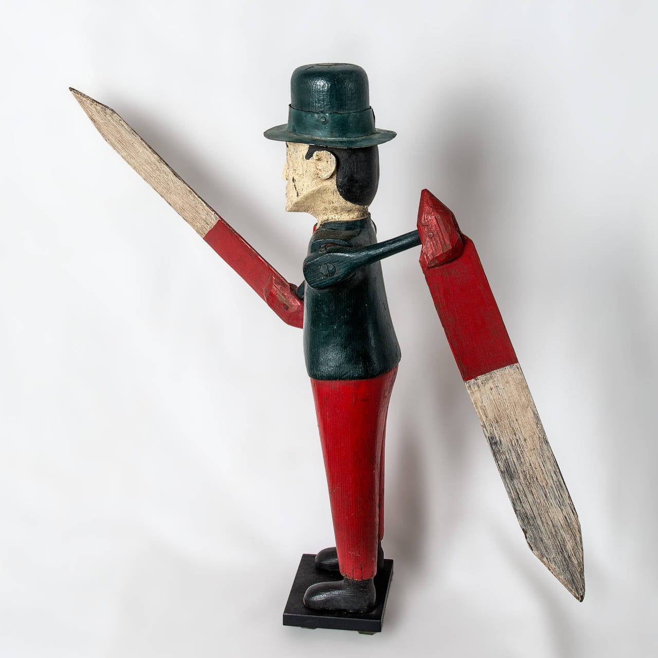 A patriotic whirligig, folksy figural carving of a man dressed in a blue jacket, red trousers, wearing a blue brimmed top hat. Painted red and white arrow style paddles.