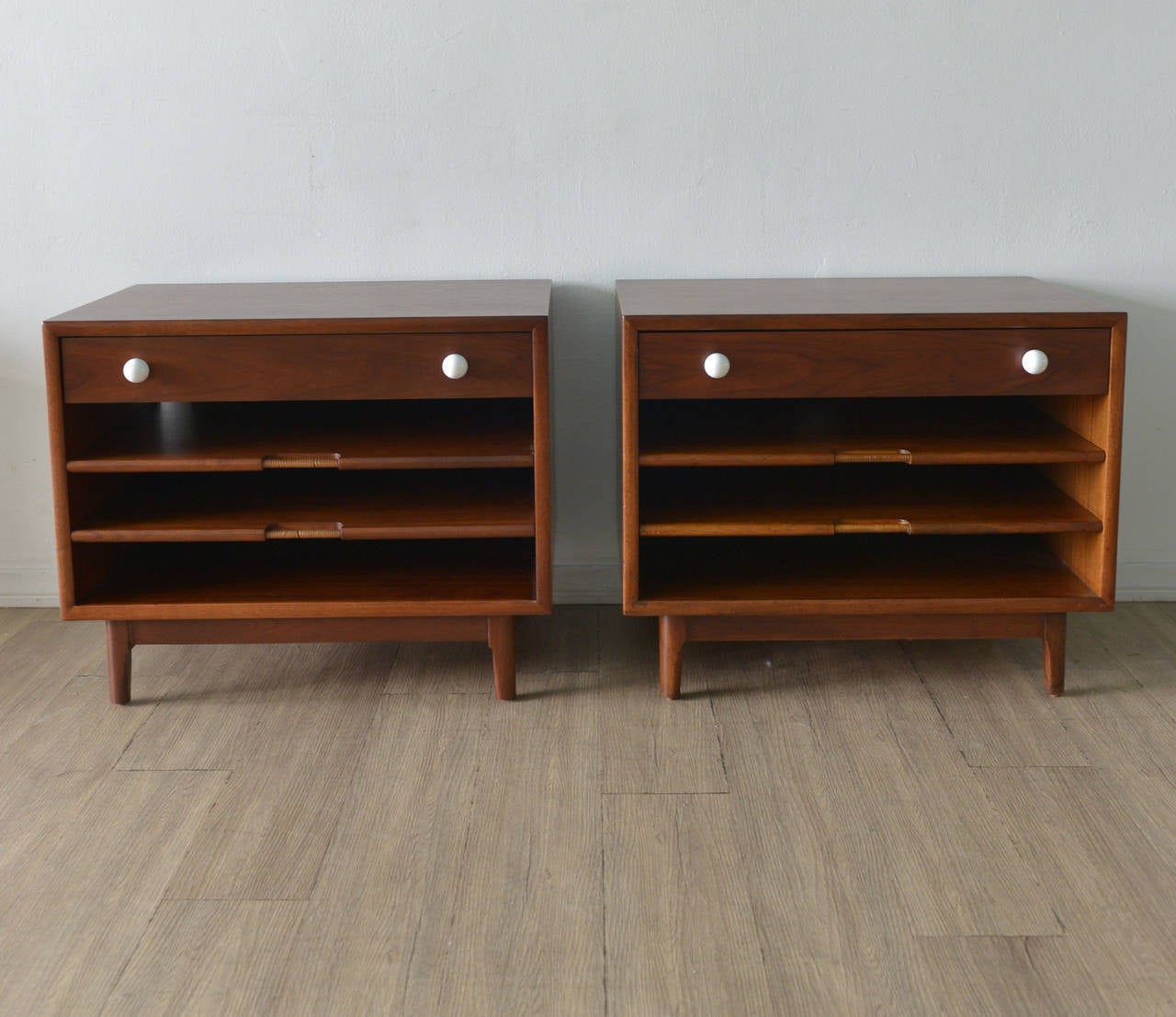 These walnut side magazine tables by Kipp Stewart for Drexel have been professionally restored and in perfect showroom condition. The pull out shelf handles are wrapped in cane for a nice finish. Unique and very functional pull out drawers for