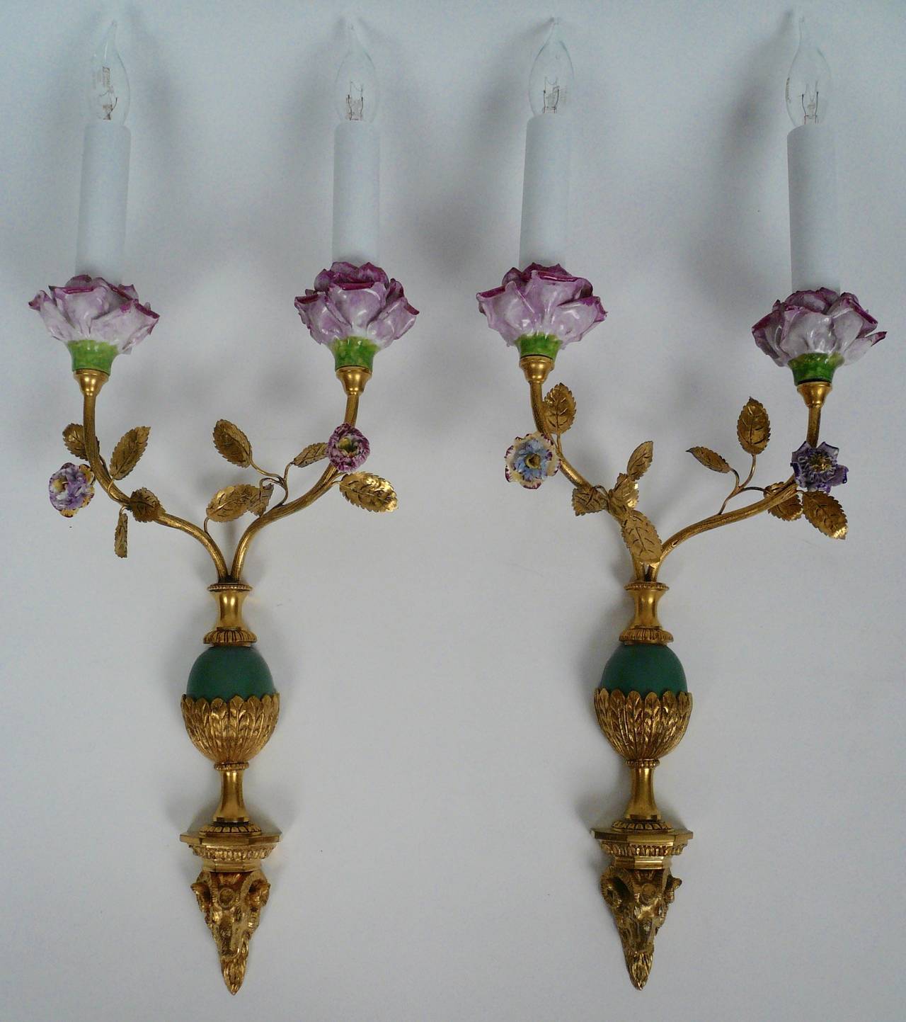 Pair of fine, two-light sconces by Edward F. Caldwell. The ram's head form bracket supports an urn shaped vase issuing curved stems that culminate in porcelain flowers, and rose form candle cups.