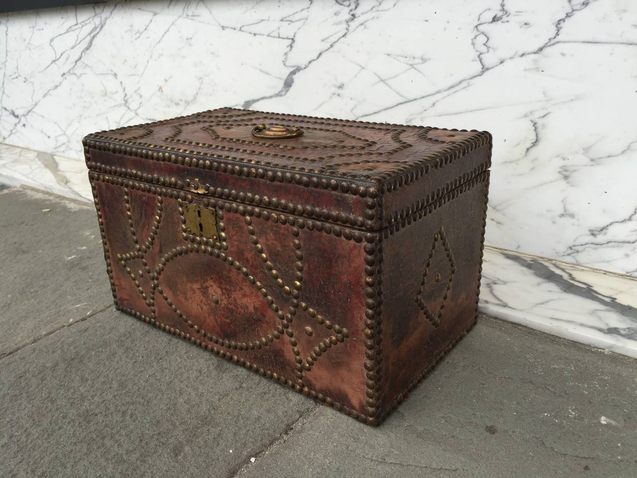 Small leather ornamented box with brass pull on top.  Paper lining on interior surfaces