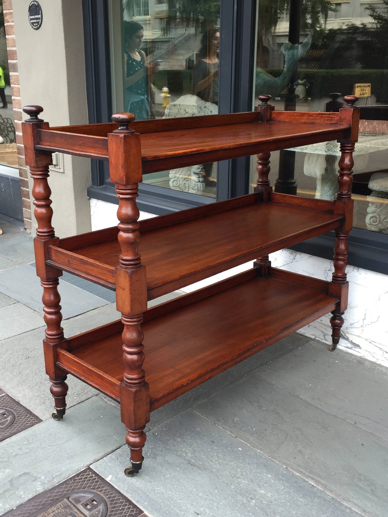 English mahogany three tier trolley on brass casters.  Turned columns support three shelves with back and side rails on each shelf