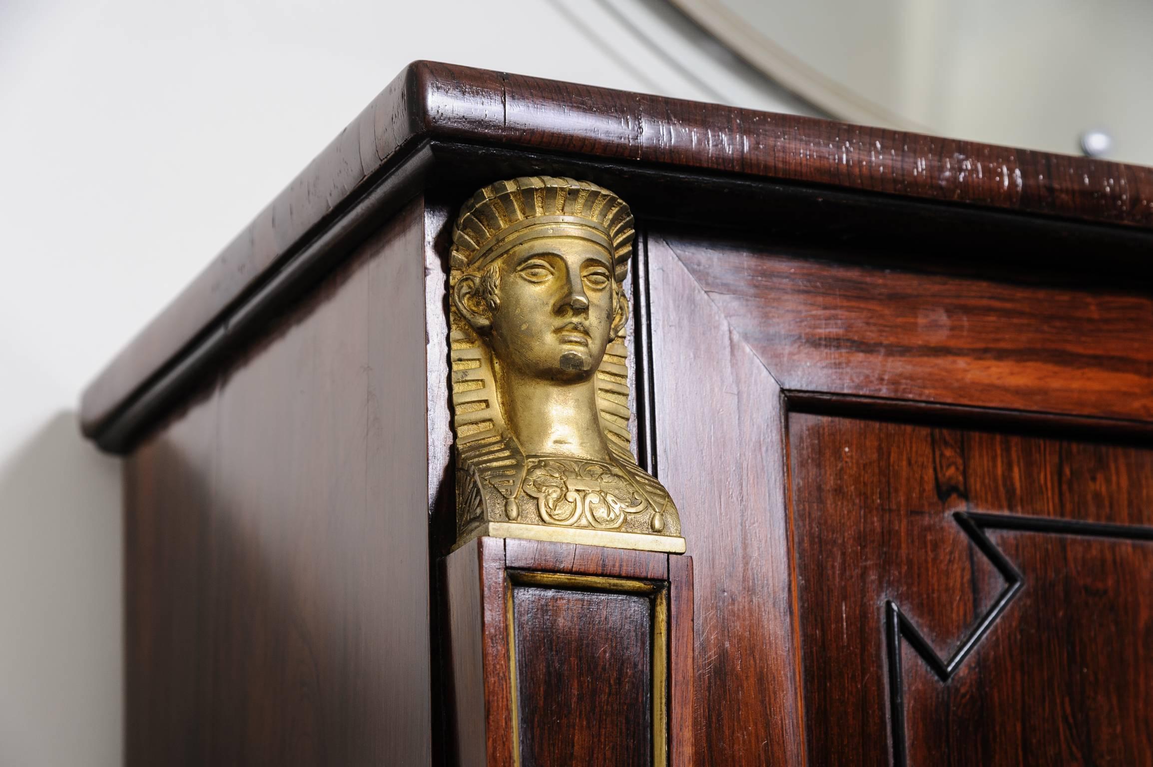 This handsome two-door r cabinet is in the English Regency style and dates from the early 19th century. The piece is detailed with Egyptian caryatid pilasters and the interior has four adjustable shelves. 

The cabinet maker was definitely inspired