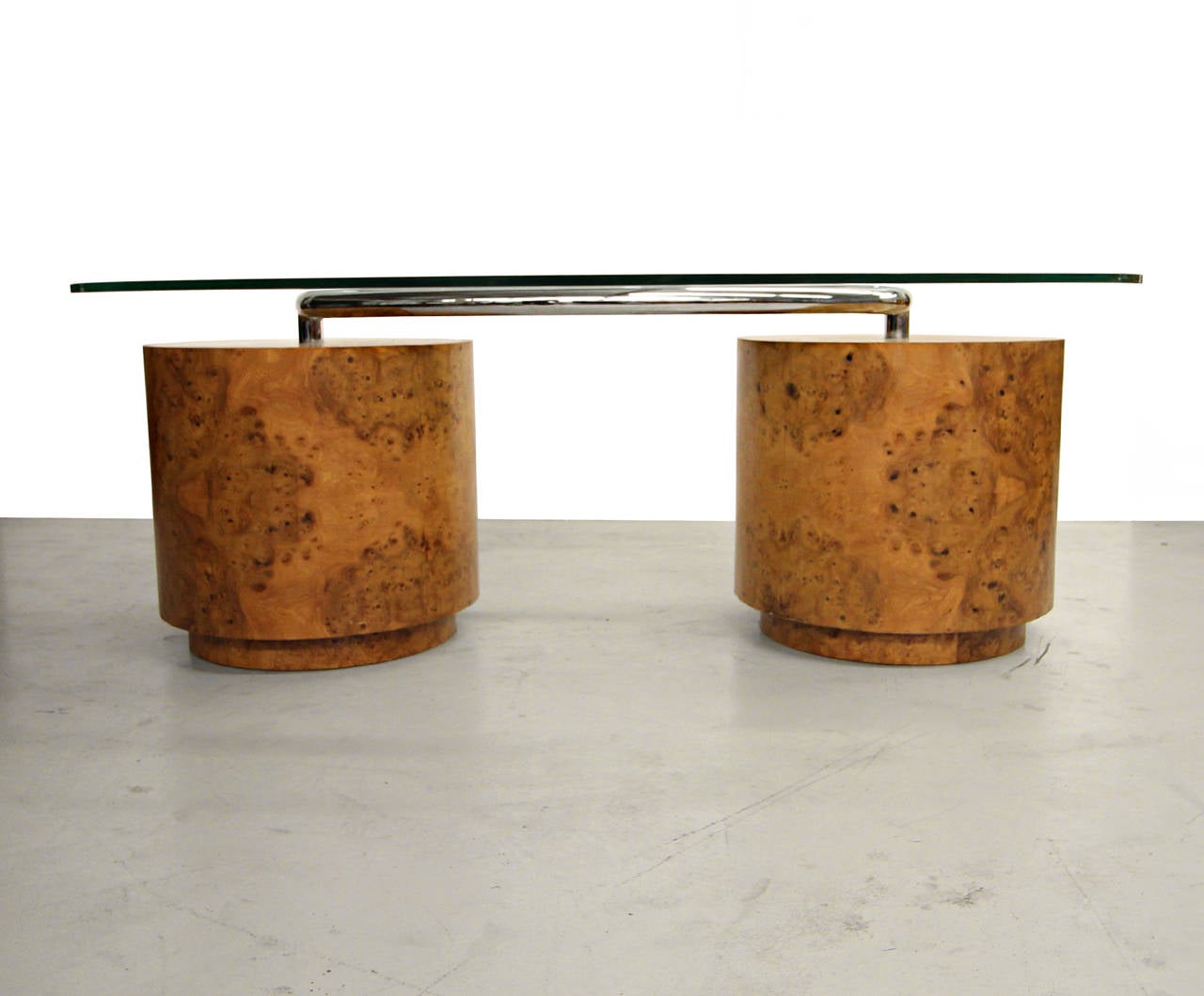 Substantial and gorgeous oval shaped Mid Century Deco Style executive desk. Desk is comprised of two round burl wood pedestals joined by tubular chrome hosting a floating glass top. Each pedestal has a set of drawers with expertly crafted cherry