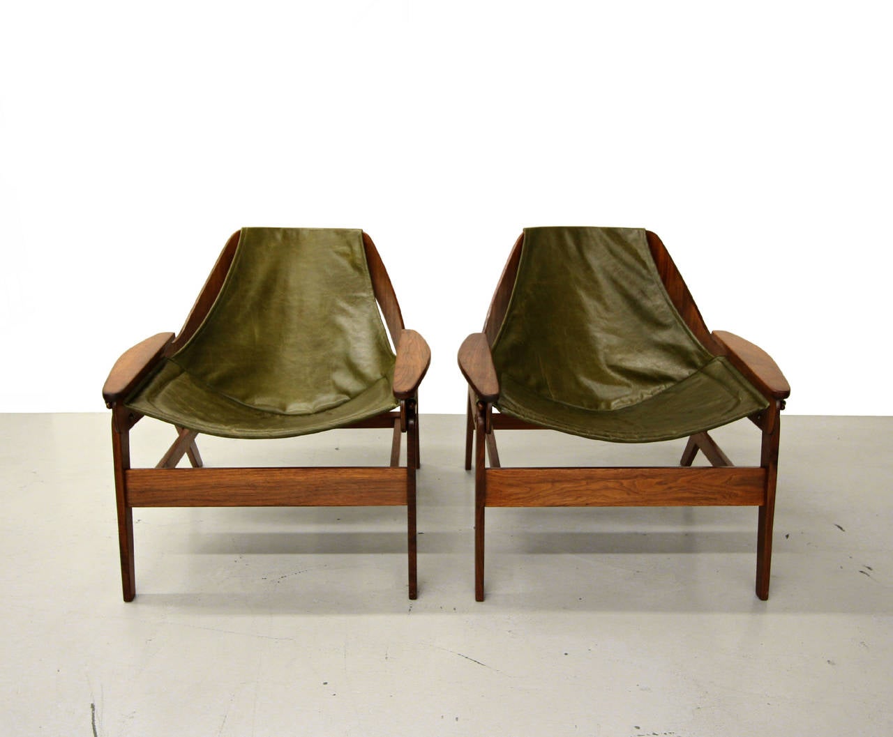 Beautiful pair of Jerry Johnson walnut and leather sling chairs.  The chairs feature beautiful sculptural frames and newly upholstered dark green slings.  These chairs are the epitome of mid century seating.  More like art than chairs really.