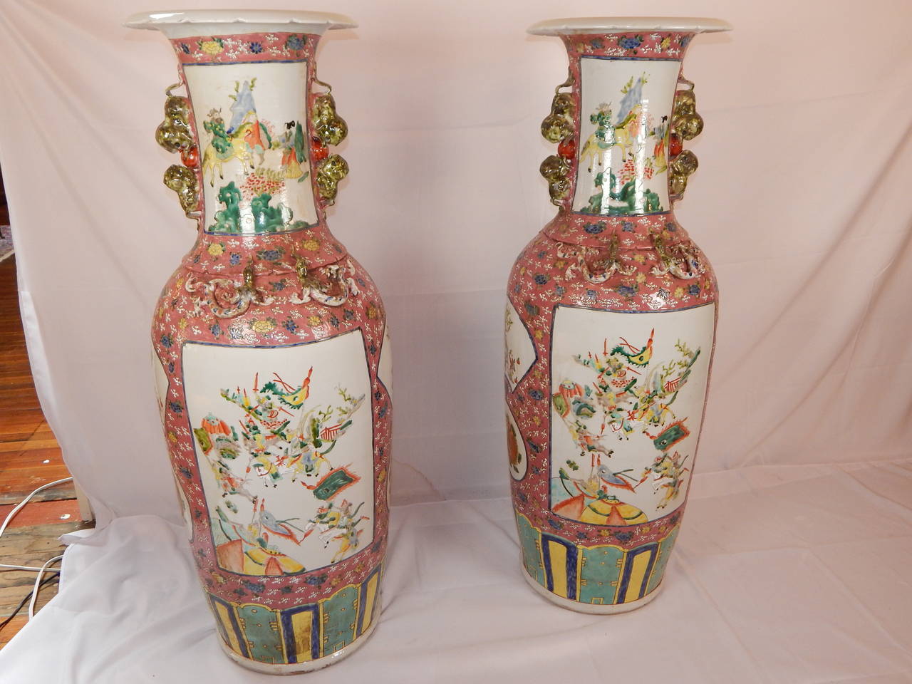 A beautifully hand painted enamel pair of Chinese palace vases, with scenes on front and back, on a pink ground, along with Foo lion handles and lizards.