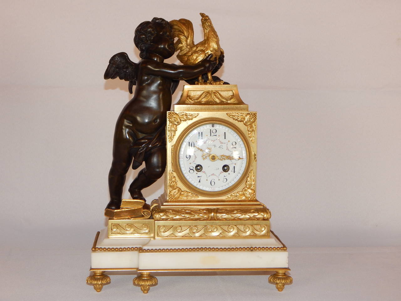 A very fine quality Louis XVI style bronze and white marble clock set in the Louis XVI style. Exquisitely modeled, this is a large, heavy and finely detailed set. It features a putto standing on a pile of books, playfully grabbing a cockerel or
