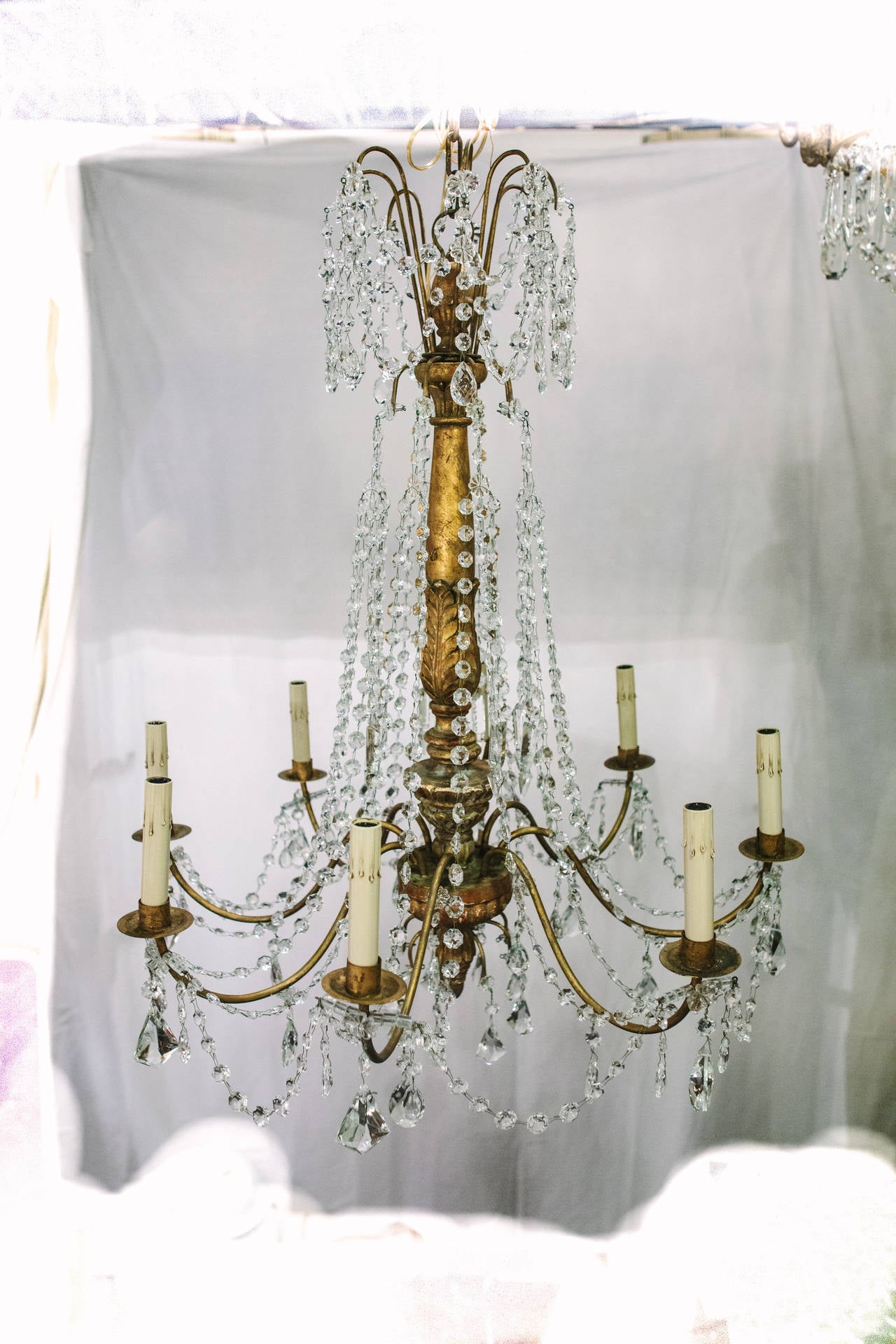 This 19th century Italian Genovese chandelier features a giltwood carved acanthus leaf center with eight iron arms projecting out. Between each of the arms are crystal swags with hanging drops. This piece originally held candles but has been newly