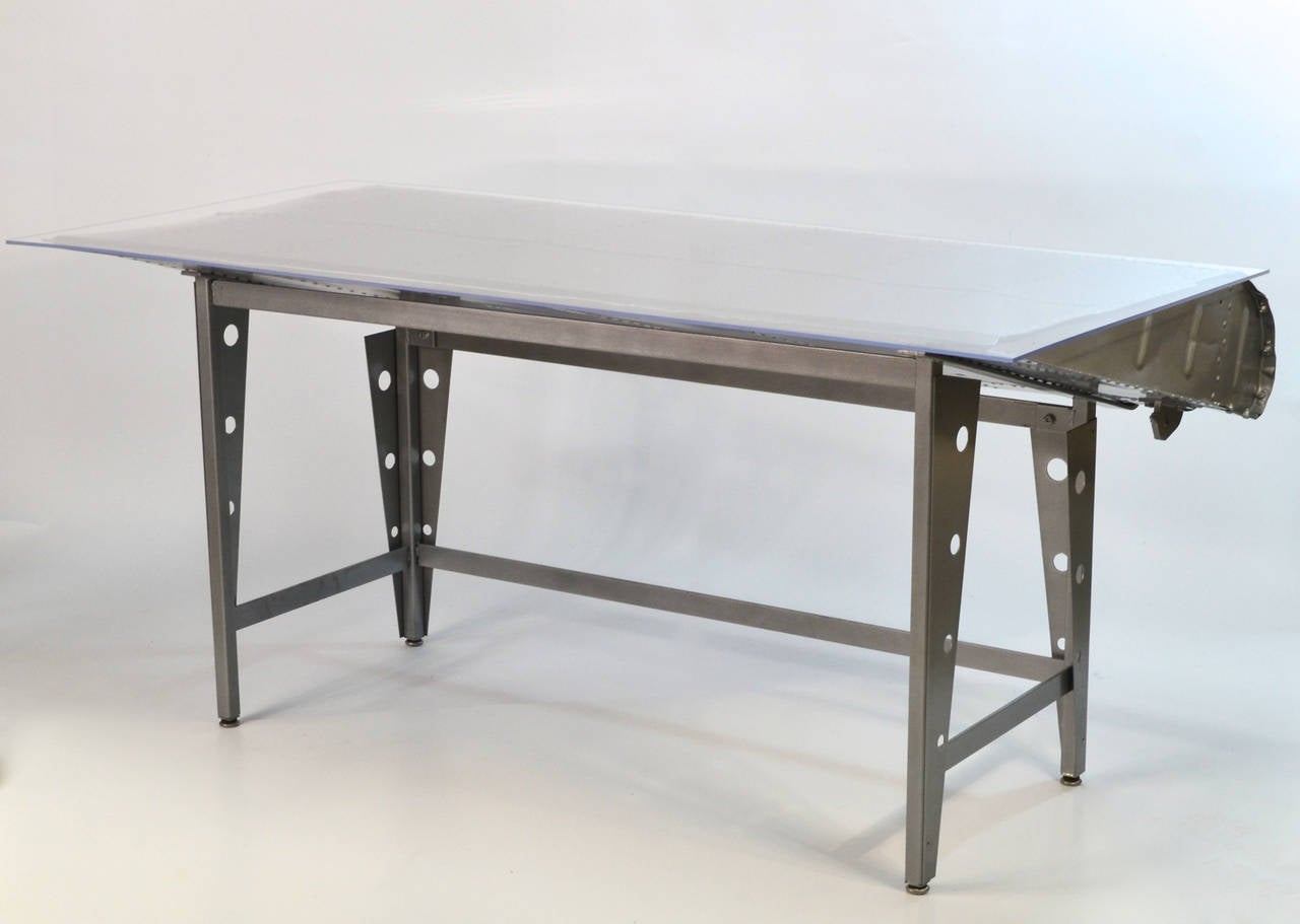 This desk is made from a section of wing from a WWII US Army Air Corp DC-3

It has a acrylic top with a silver powder coat paint finish. Beautifully constructed. Truly a once in a lifetime opportunity to own a historical airplane artifact. 