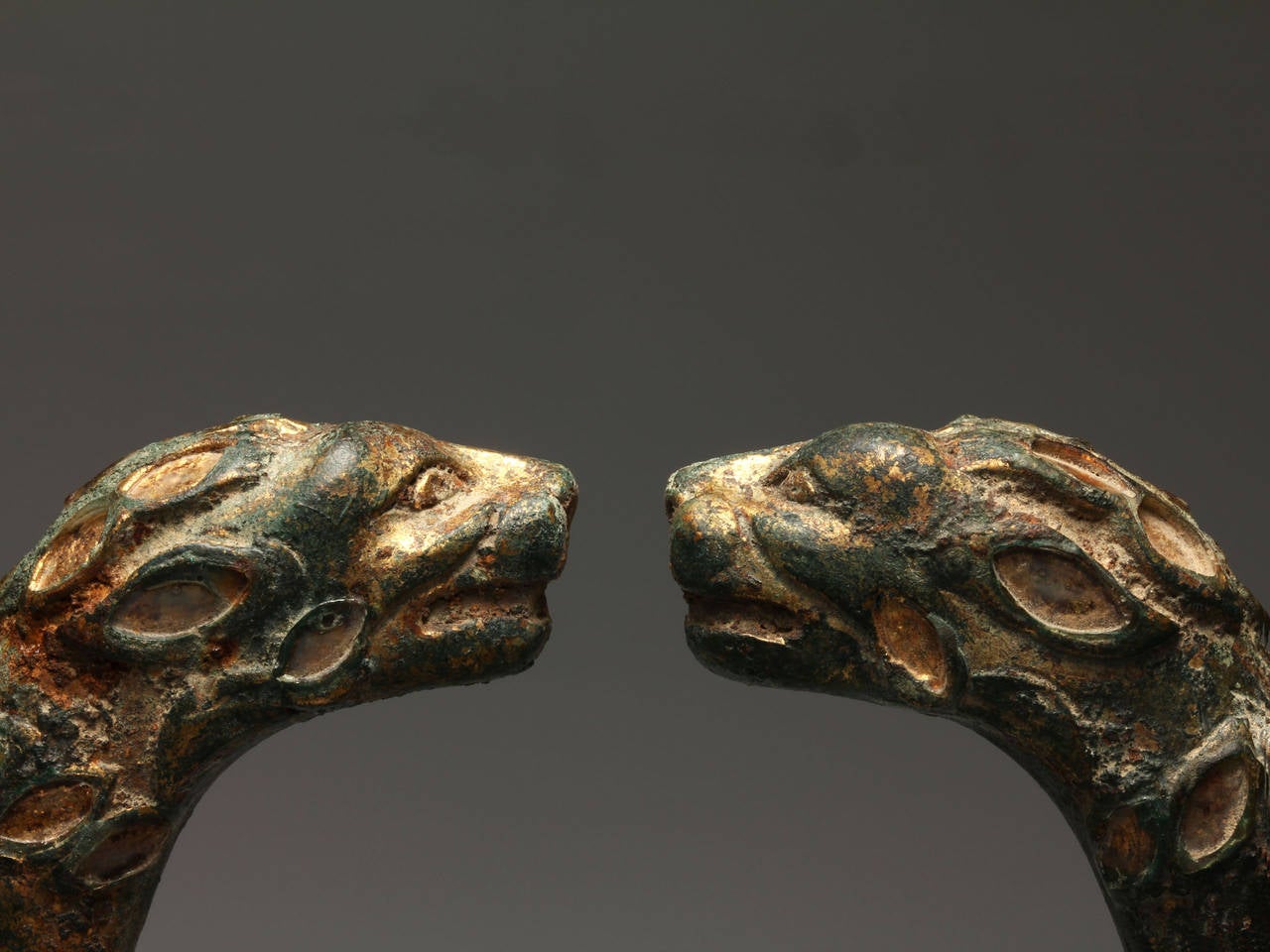 The solid penannular hoop terminating in two confronting lion heads, with snarling open mouths, decorated with incised petal-shaped markings filled in niello-like inlays, some of which are preserved. Weight: 377g. Mounted

Near identical bracelets