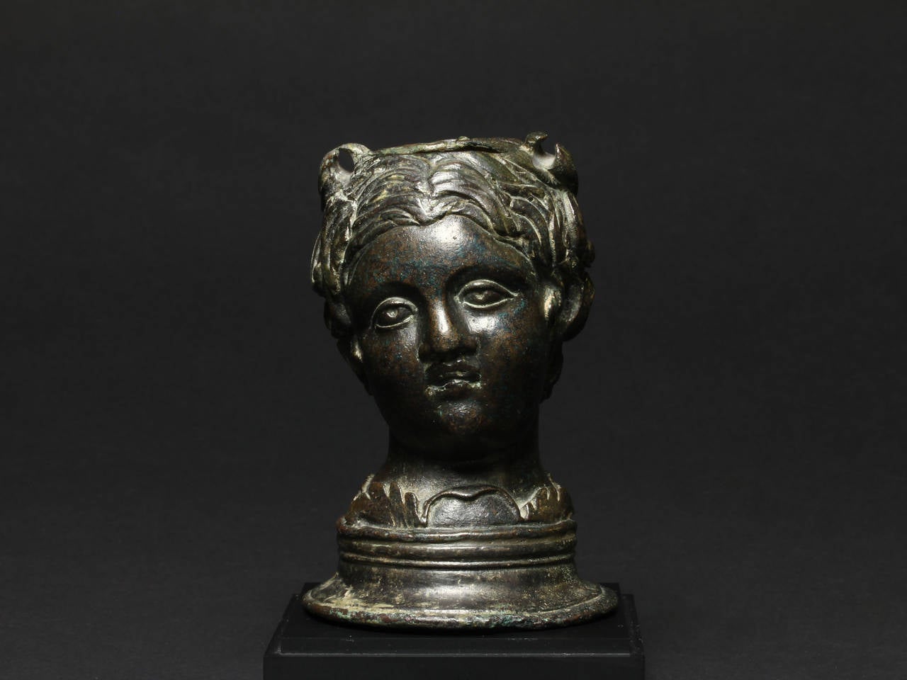 Depicted emerging from a wreath of vine leaves, the naturalistically rendered and finely modeled bust of a young boy with its head slightly titled right, composed of thick comma-shaped locks and frontal centrally parted hair, his large almond-shaped