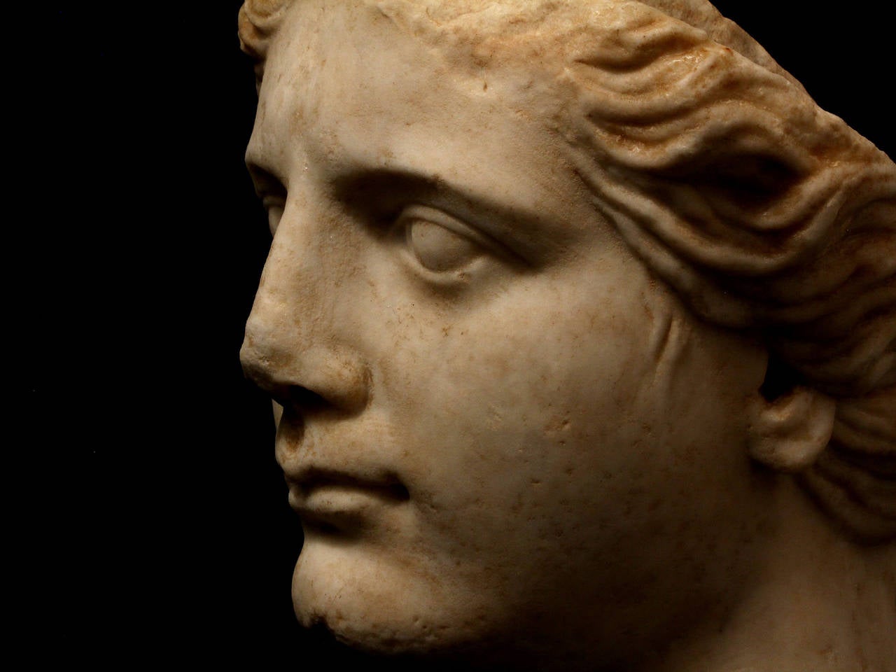 The top of the goddess's head is cut-off with a raised rectangular tang for attachment of her helmet, once separately carved and now missing, her waiving hair centrally parted and drawn back towards the base of her neck, the remnants of an iron pin