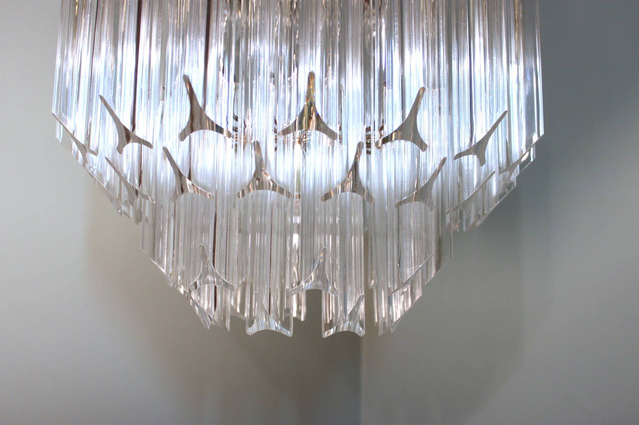 This lovely and dramatic 1960s Lucite and brass chandelier emits a beautiful light, with all the reflections in the four tiers of Lucite prism, which are triangulated and cut on an angle. The brass frame that supports the Lucite prisms has five