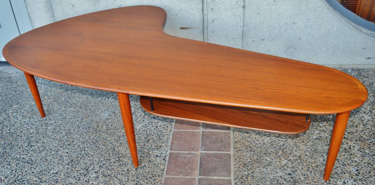 This sexy Danish Modern teak coffee table has totally killer lines and styling, with it's organic boomerang shape. Even the pair of matching side tables are organic in their being trapezoidal in form. Featuring a softly contoured top edge, gorgeous