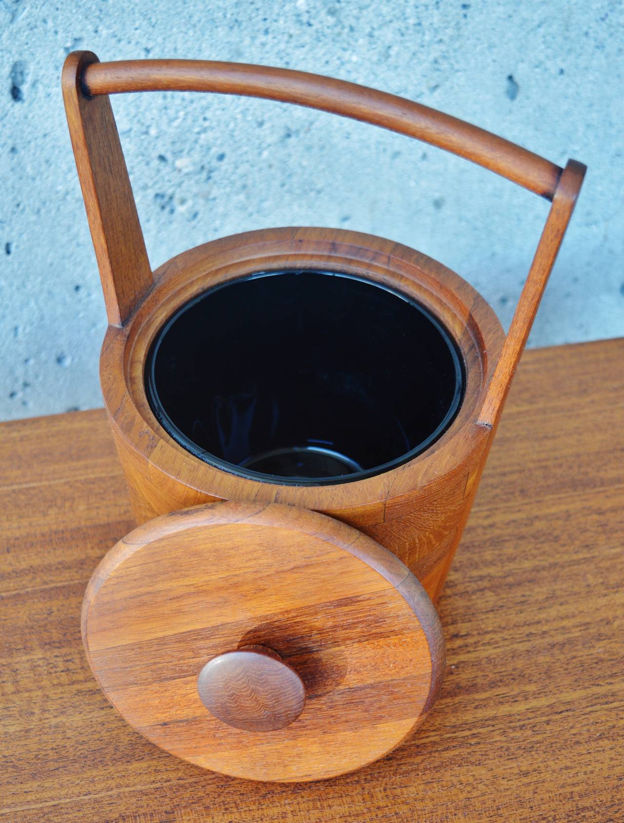 This rare model Danish Modern teak ice bucket by Jens Quistgaard is charming and beautifully crafted. Made of solid teak wood in a mosaic pattern with the handle merging into the bucket with a lovely flare. The insert is made of black glass. In