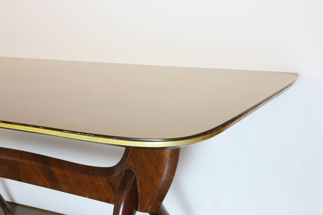 Mid-century modern wood and glass top dining table, design attributed to Vittorio Dassi (Milan, 1893-1973), stretcher base and shaped legs supporting a large glass top with greenish-gold painted underside. Some scratches to glass top and loss of