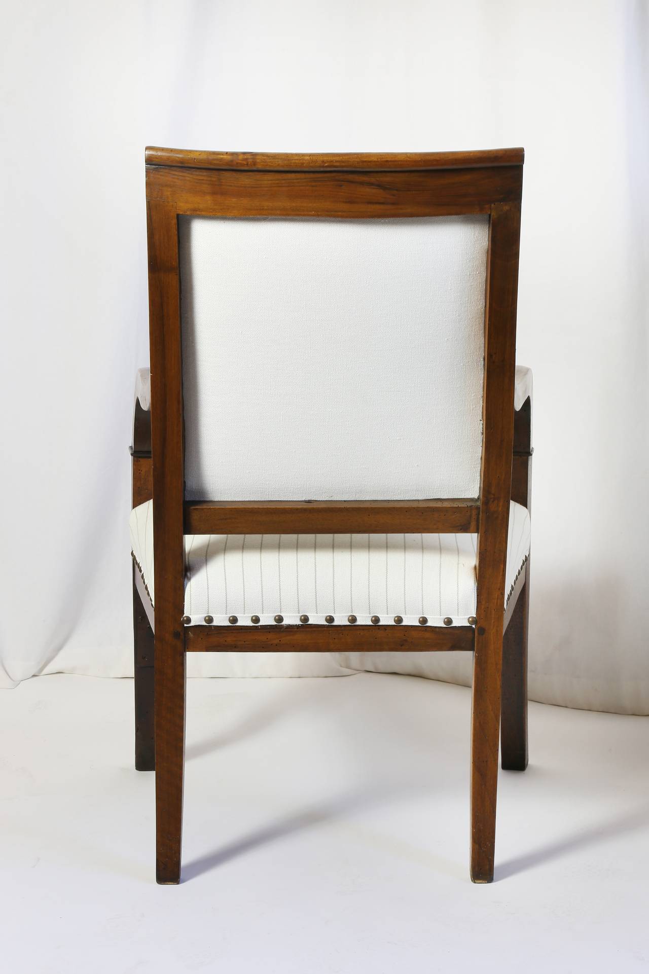 French Provincial walnut arm chairs, the crest rail over the upholstered center back and seat with framing arms extending to the slightly curved legs. New upholstery in striped linen with nail head detail.