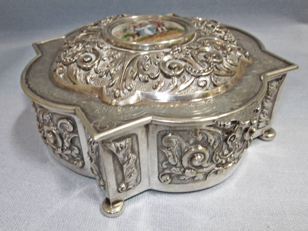 This lovely jewel box is made of 83% silver and is so marked.  The porcelain inlay is a transfer design with a few brush strokes of real painting.  
Lovely vintage piece with a nice patina to the silver.  No key comes with it so we do not know if