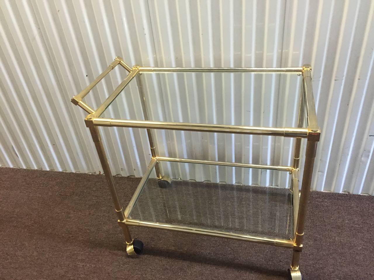 A vintage 1970s brass framed bar cart on casters with two glass shelves. Good vintage condition with age appropriate wear and patina.