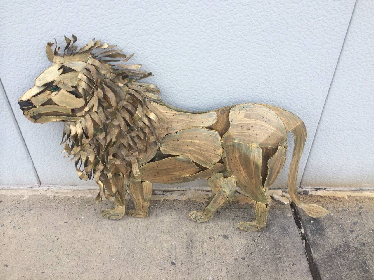 A Brutalist multi-dimensional wall-mounted lion sculpture, circa 1966 made of gold patinated  Metal with a green faceted glass eye. Signed on the back Tessa and Leroy, 66.Would Be Great in your High End Jungle Den Interior.