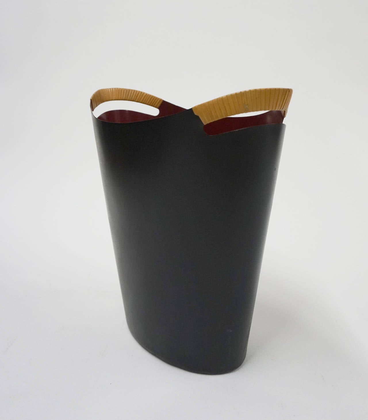 Enameled metal wastepaper basket with cane wrapped handles by Grethe Bang for Torben Ørskov & Co. Black enamel exterior and dark red interior.