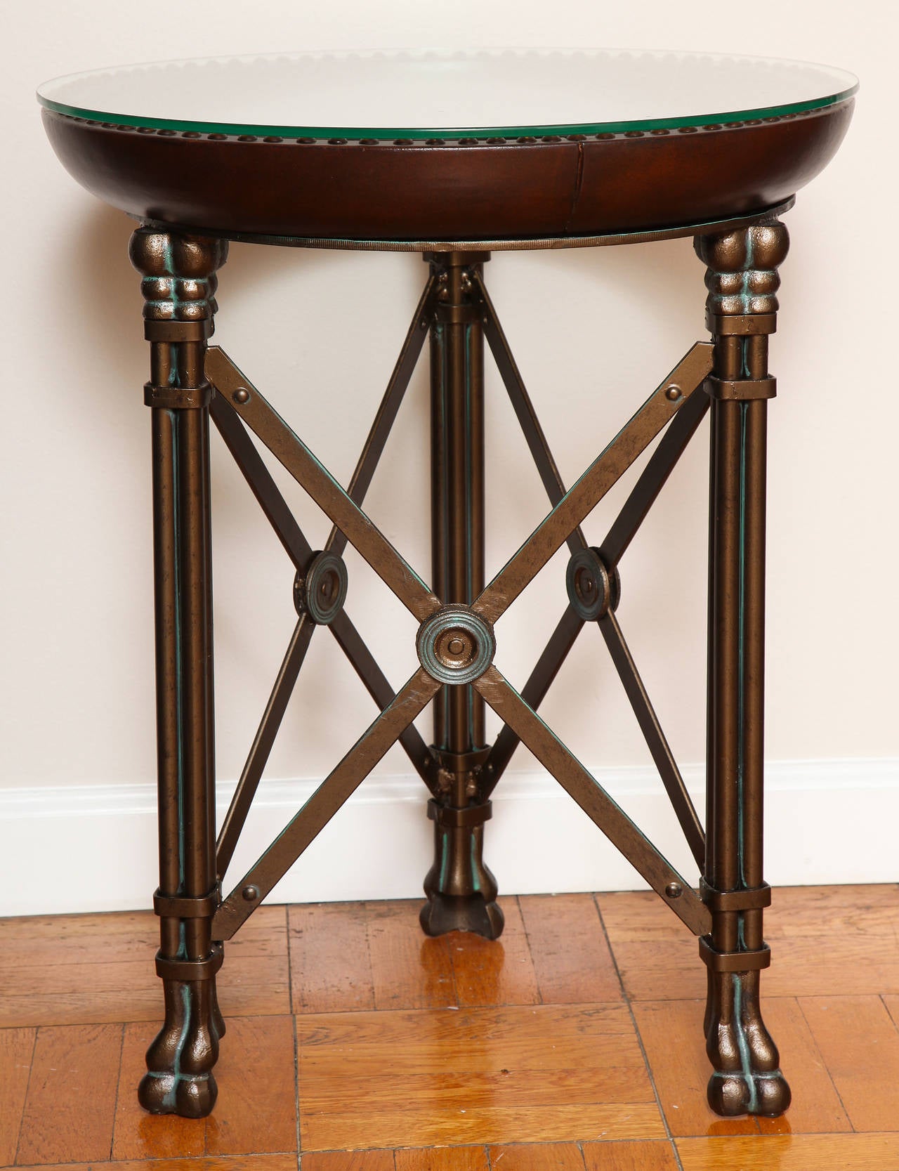 A pair of round side tables by Maitland-Smith; the drum tops in deep brown leather inset with 2 tiers of original glass tops resting upon three columnar brass legs with lion paw decoration; with enameled steel X stretcher between each leg.