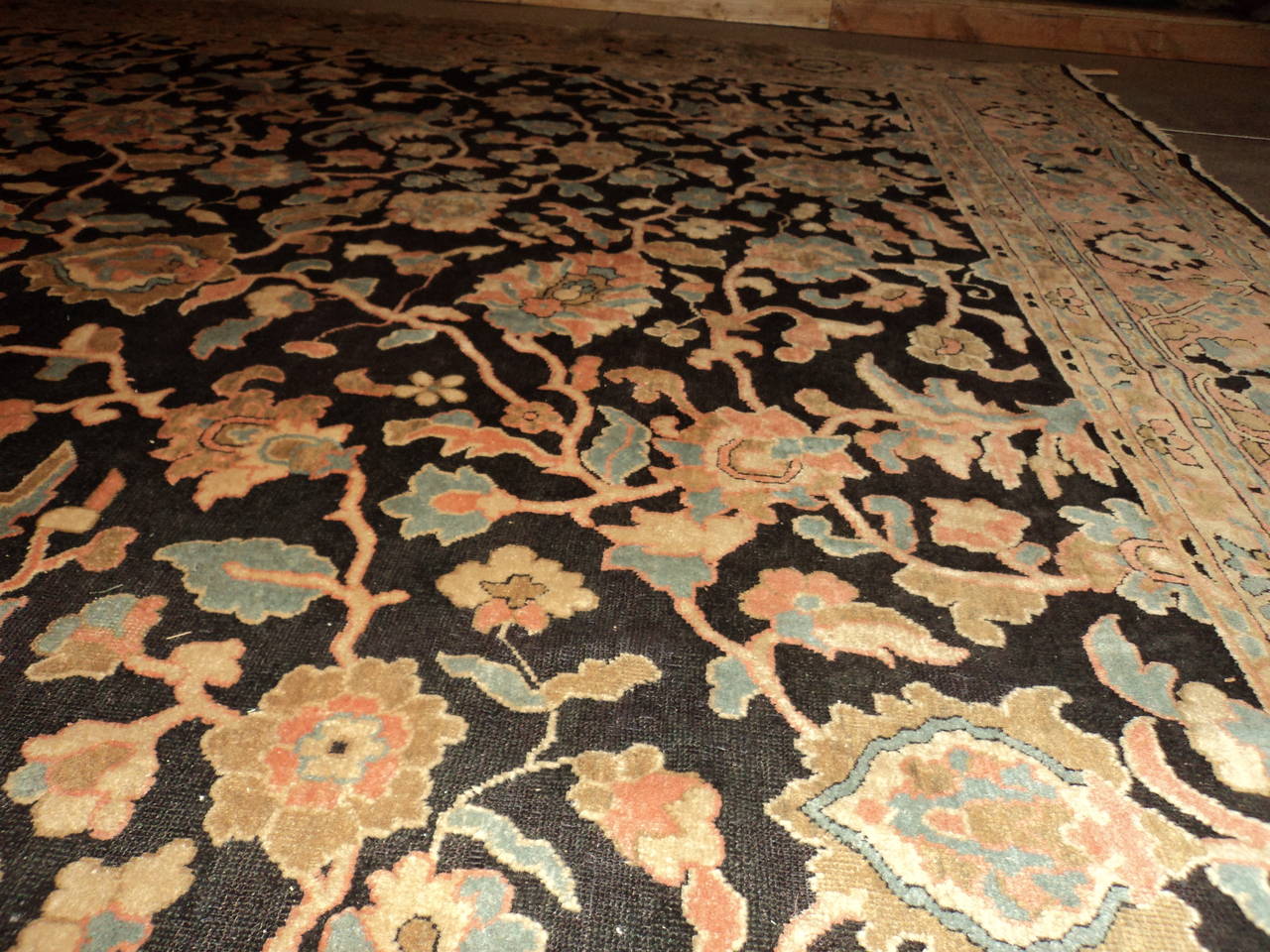 This third-quarter of the 19th-century Agra from India Oriental Rug measures 11’1” x 15’3”. It has a black background with a vine and tendril design in coral, very pale sky blue, ivory and mocha brown.  The vine and flower motif is quite large and