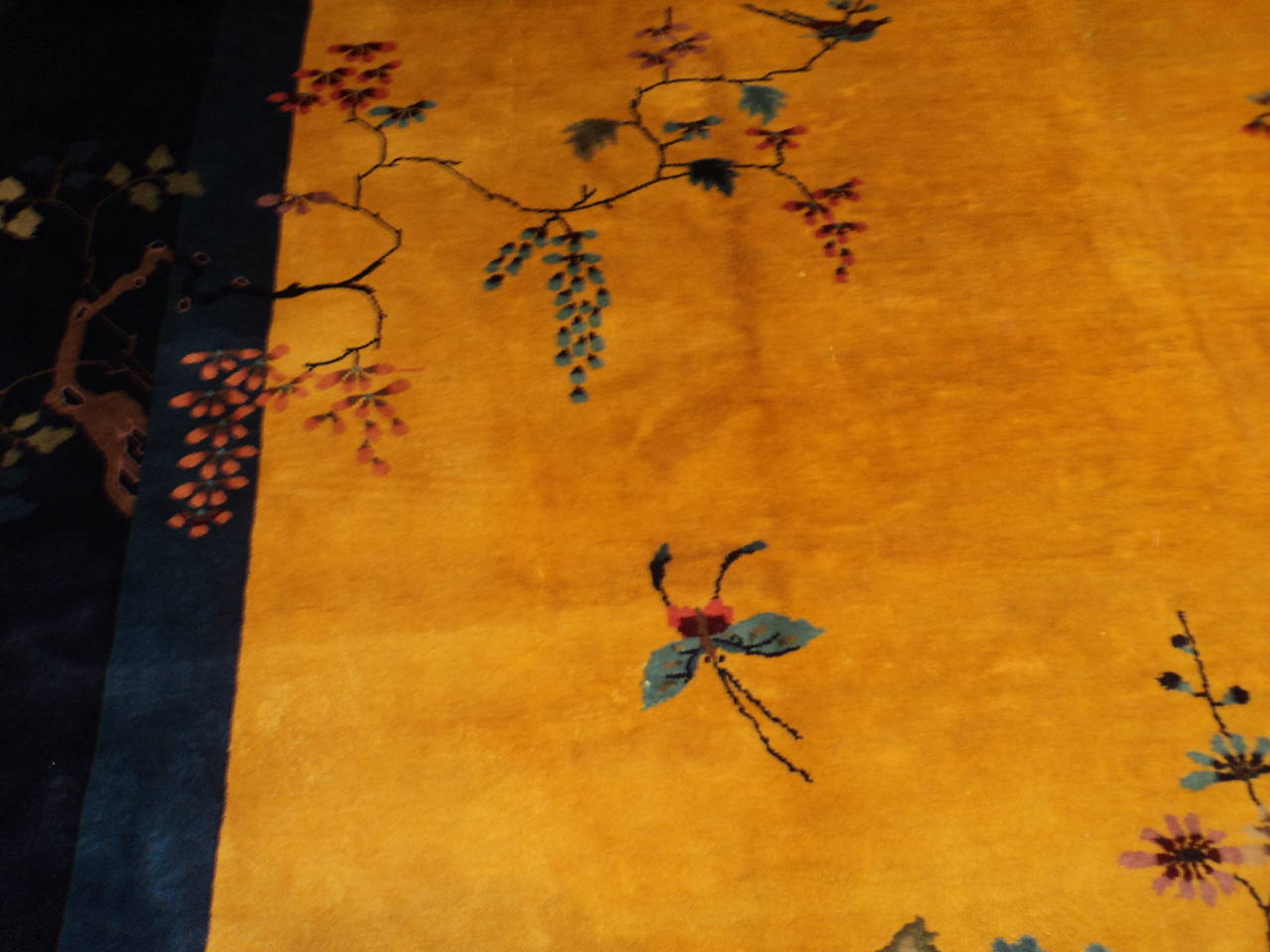 This circa 1920 Mandarin Chinese Art Deco Oriental Rug (INV 7541) measures 10’0” X 13’3” (304 x 405 cm). It has a yellow gold field with a floral motif in purple, three shades of blue, maroon, black and touches of green. The motif comes in from the