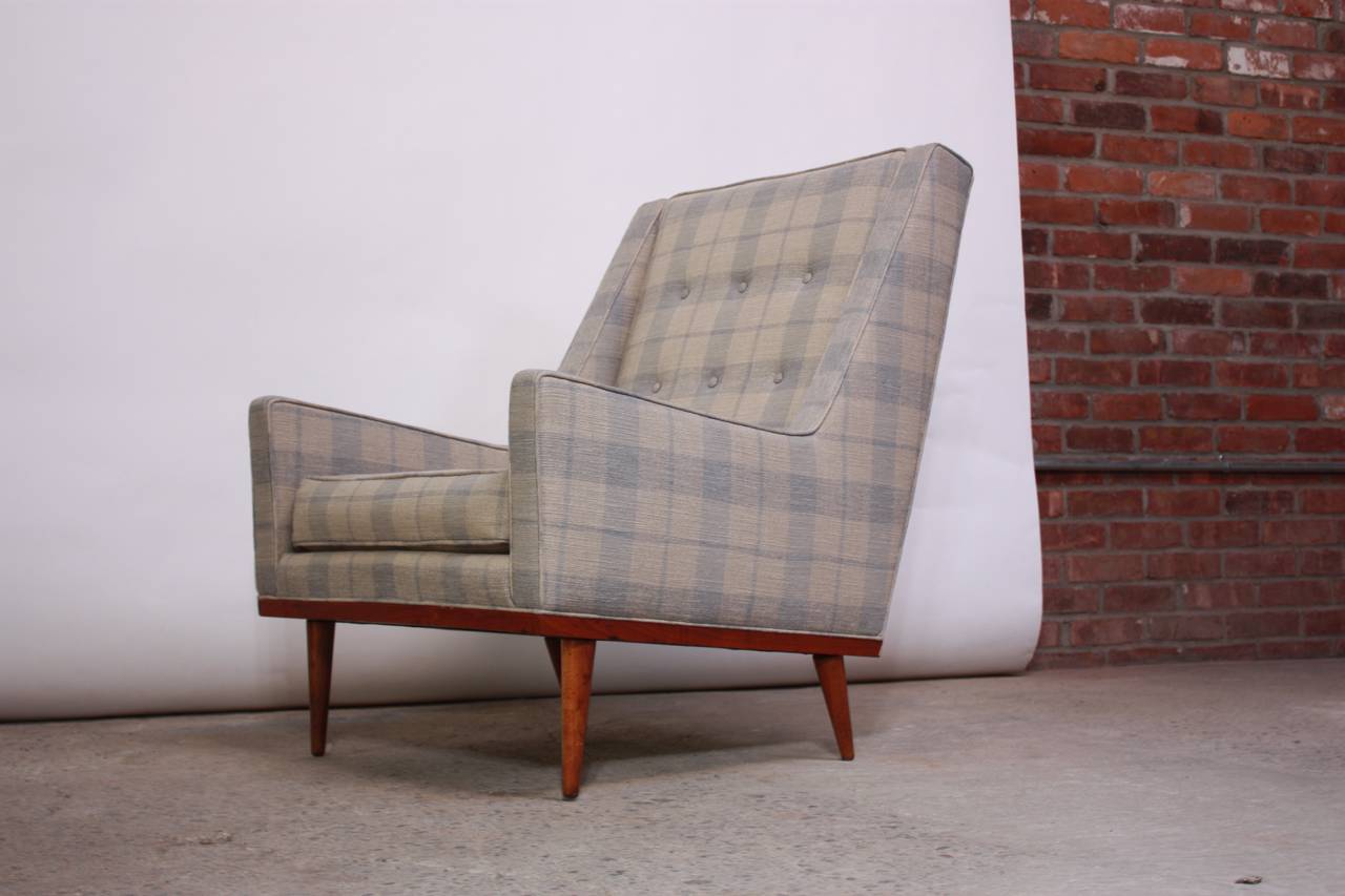 This handsome Milo Baughman lounge chair is an early example of the work he designed for James Inc. The base frame and legs are walnut. The sharp, clean lines and high back define the piece giving it a statuesque presence. The plaid upholstery is