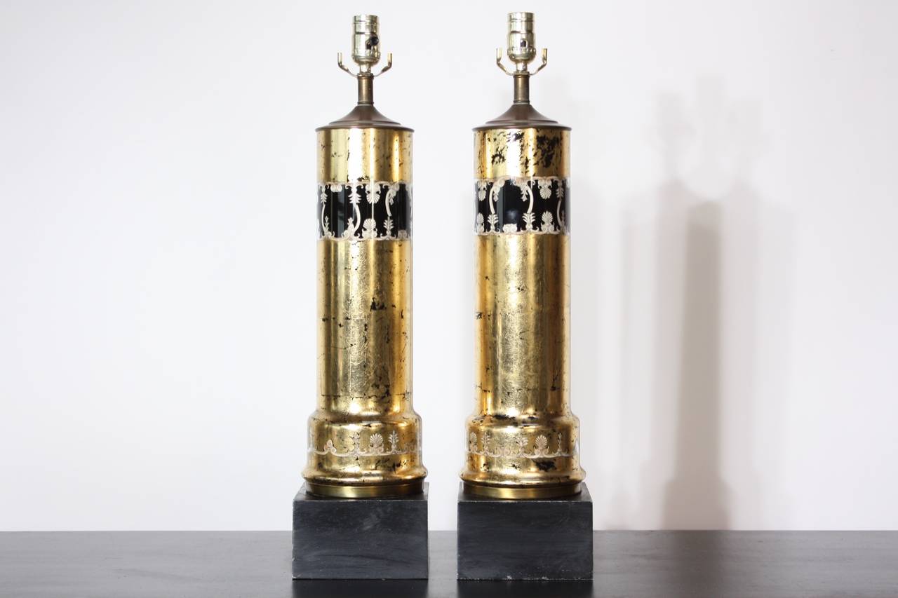 These Italian Mid-Century Modern table lamps were constructed using reverse applied gold-leaf and transfer printed lithographic design encased in glass on black lacquered square metal bases. The caps to which the sockets are mounted are bronze.