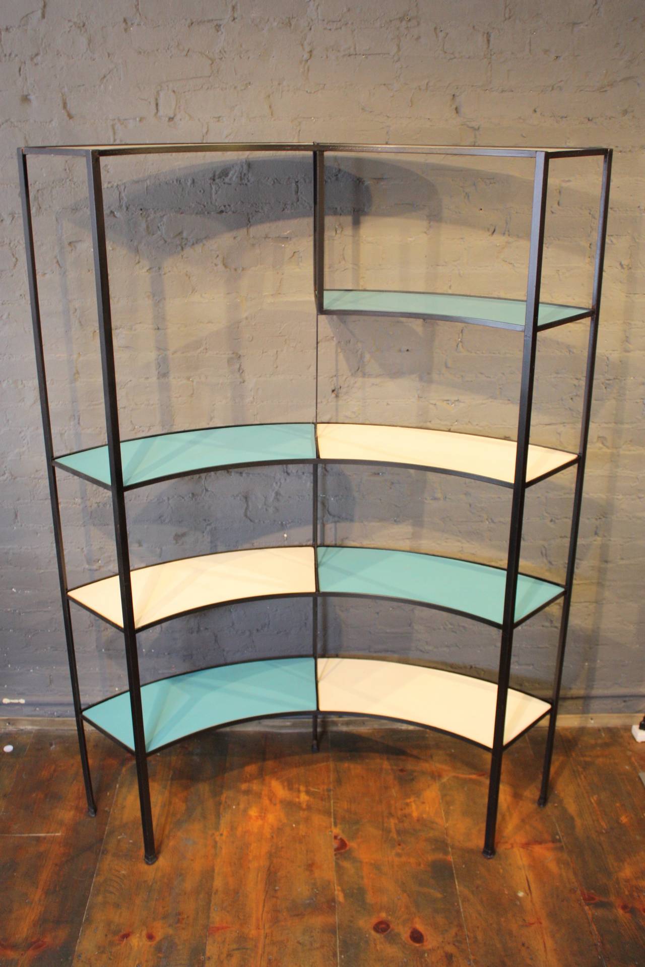 This rounded shelving unit was designed by Frederick Weinberg in the 1950s and is comprised of a wrought iron frame and blue and white masonite inserts.
There is age-appropriate wear to the original inserts (mostly to the edges where the iron meets