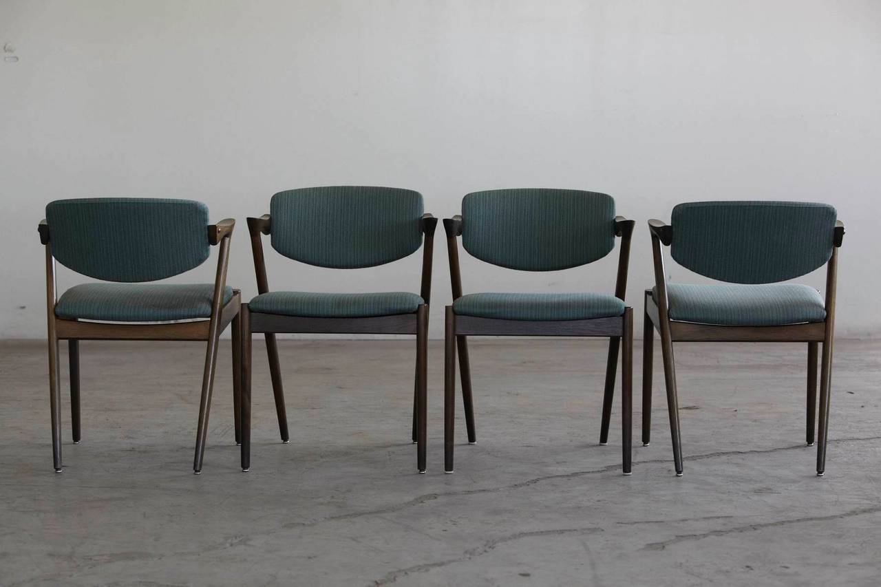 Set of four 'Z' dining chairs designed by Kai Kristiansen, model #42. Features a solid oak frame factory stained in a slight green tint with tilting backrest and dramatic angled half armrest designed for comfort and functionality. Original, matching