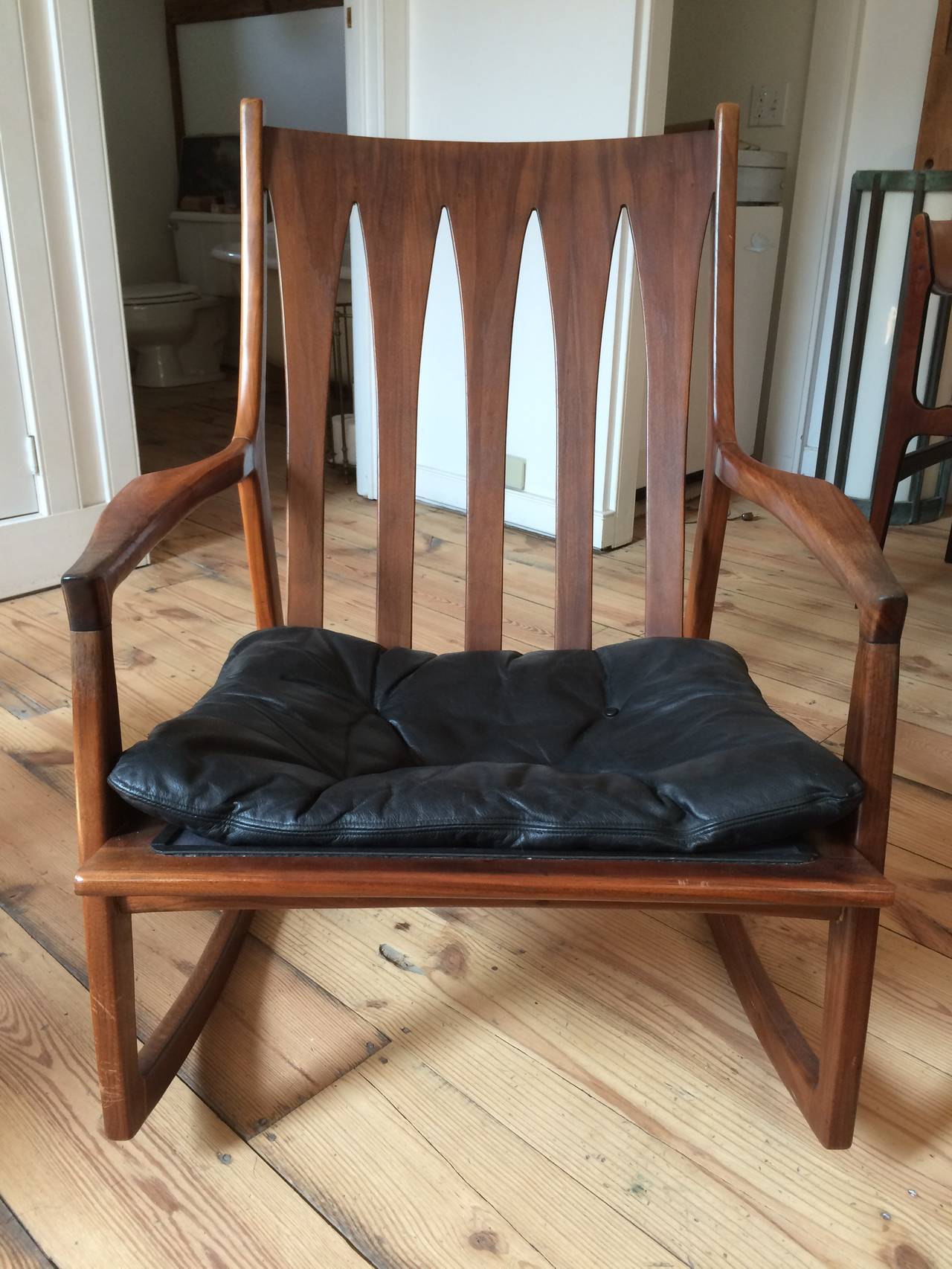 A supremely wide masculine rocking chair with original black leather seat cushion. It could do with a little restoration of the wood as seen by the photos of the arms, but it's a really exceptional rocking chair.