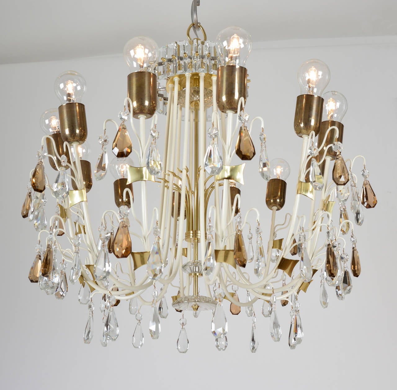 Delicate crystal chandelier of polished and white varnished brass. Pendant crystals on the arms and rare band of rectangular crystals at top. White anchor-shaped frame with playfully placed contrasting brass details. Prominent crystal centre parts