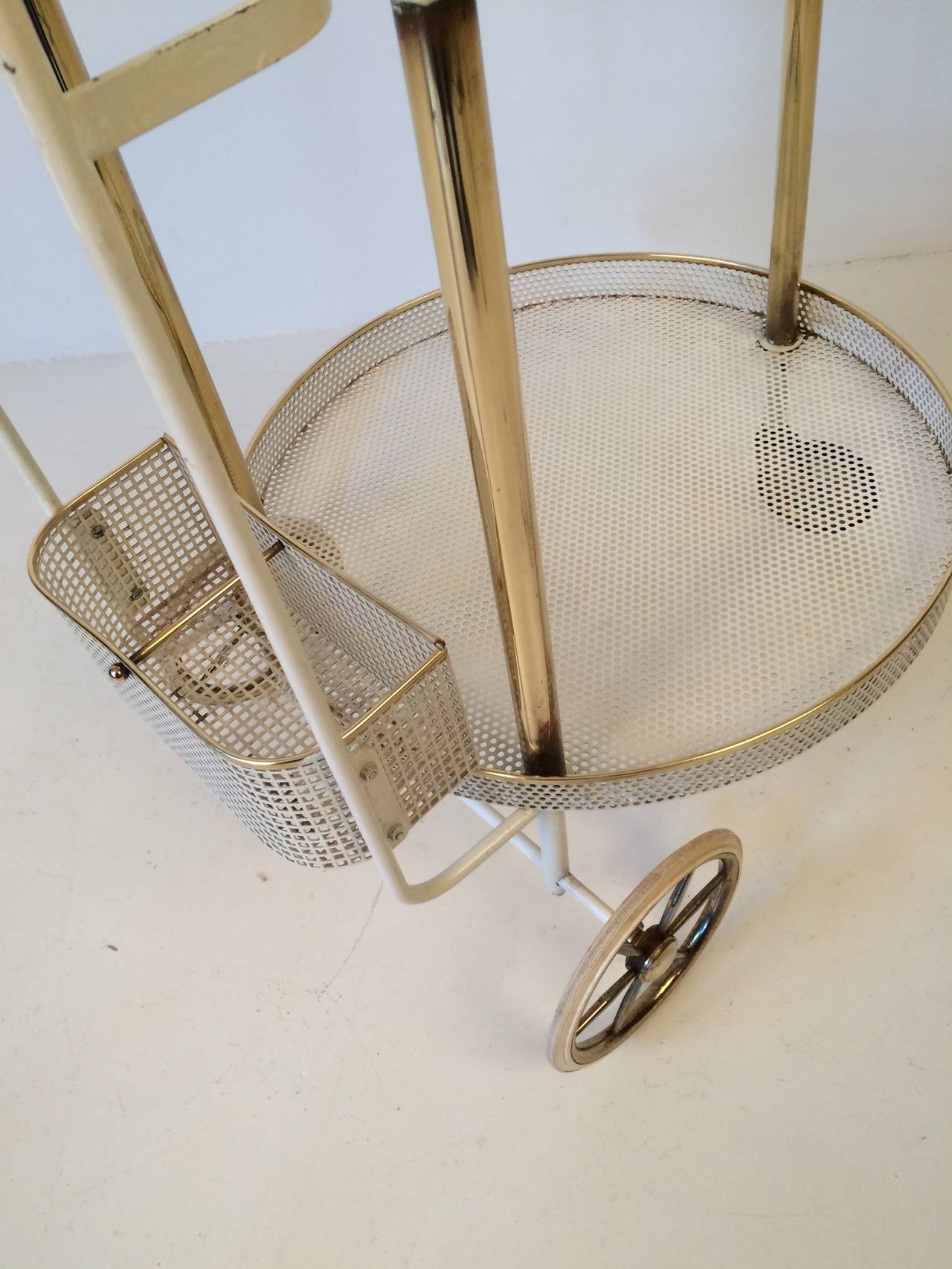 Beautiful 1950s white, gold and brass bar trolley.

This trolley is made of perforated metal sheets. The upper tray has a gold-plated glass inlay.

Measurements: H 84 x W 48 x D 58.