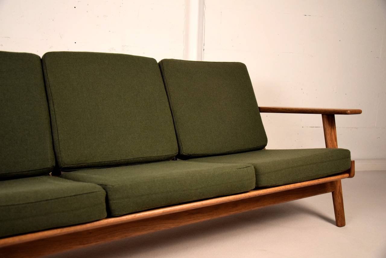 Three-seat sofa GE 290 in solid oak, Designed by Hans Wegner in 1955 for GETAMA, Denmark.

Olive green pillows in reasonable condition with some fading. We recommend new upholstery.

We also propose the matching high and low back