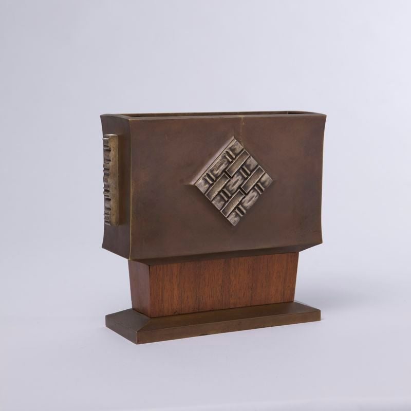 Known as ceramist Paul Ami Bonifas (1893-1967) made also bronze vessels like this one. The piece shown here is particularly elaborate with the trapezoid wooden piece joining the base to the vessel (both made of brown patinated bronze) and the four