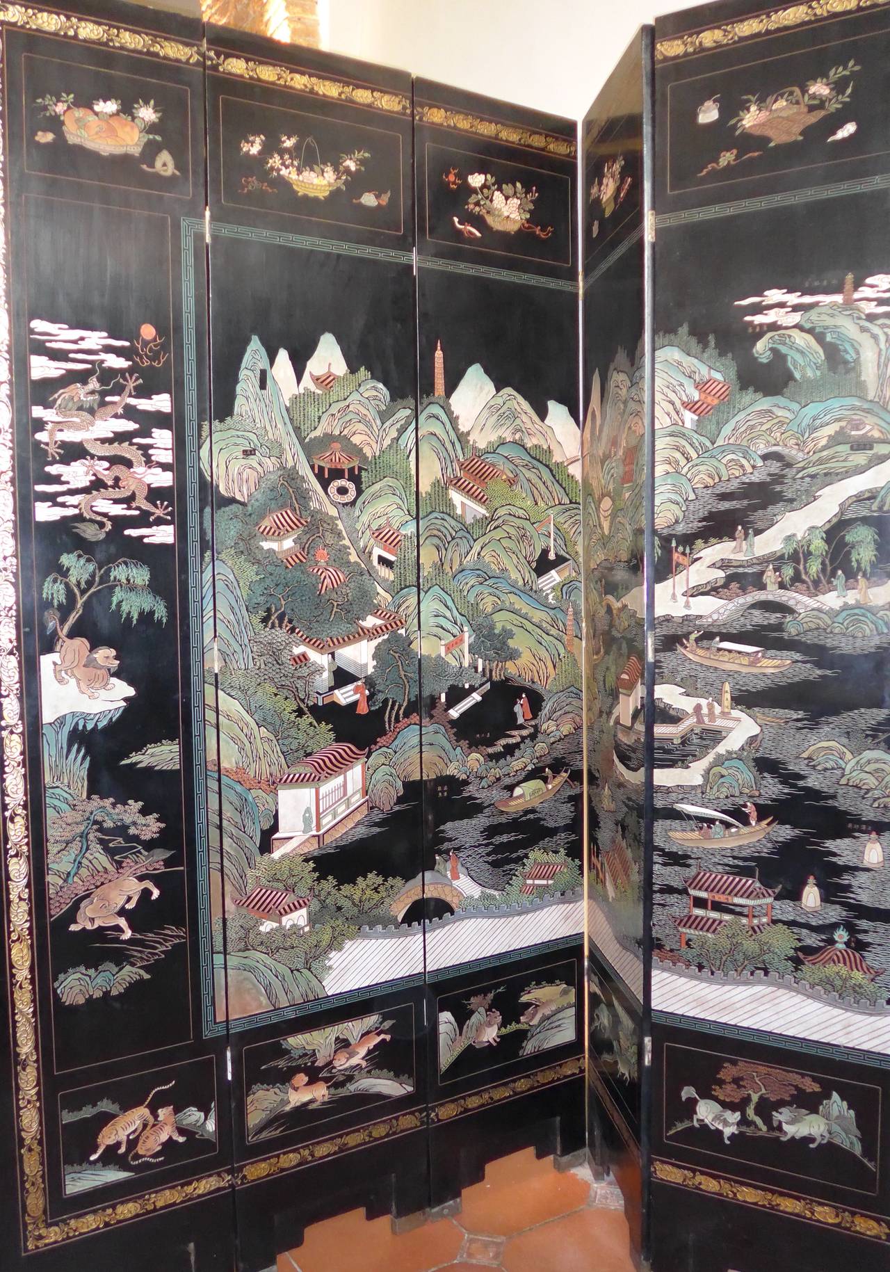 An impressive twelve-leafed Coromandel Lacquer Screen, circa 1930s carved recto with Pavilions and People in various Mountain and Lake Landscape. Framed by Mystical Beasts vignettes at the bottom and scholars item on top, verso the 10 central leaves
