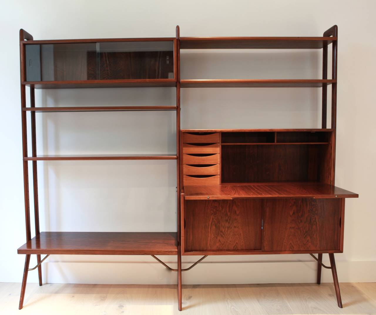 A rare rosewood bookshelf with sliding glass doors and a hideable secrétaire with small drawers and lower brass supports.
In perfect vintage condition.