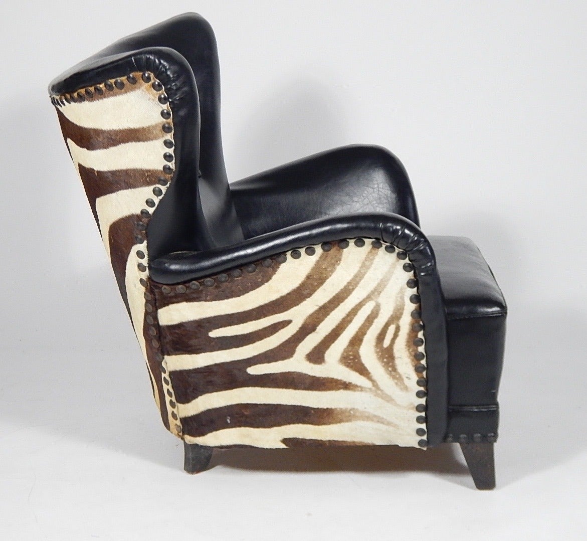Winged easy chair with stained beech legs.  Seat upholstered with black imitated deep-buttoned leather, sides and back upholstered with vintage zebra skin, studded with brass nails. Danish, 1950s or late 40s.
