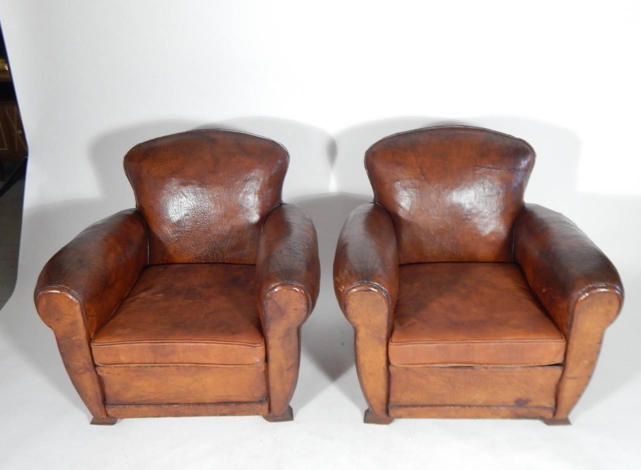 Gorgeous pair of leather club chairs from the Art Deco period. Exceptional patina, original angled wood legs in the deco style, beautifully curved back and a rare starburst stitching detail to each arm, original brass tacking to back, France, circa