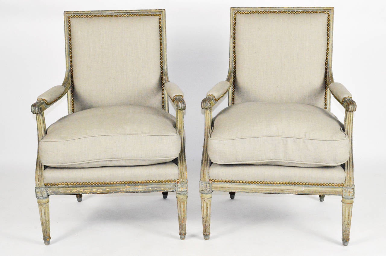 A fine pair of 18th century French Louis XVI painted bergères. Each with rectangular back and open arms. Seat with a loose cushion. Covered in linen with nailhead trim. Raised on tapered fluted legs. Having original pained finish.