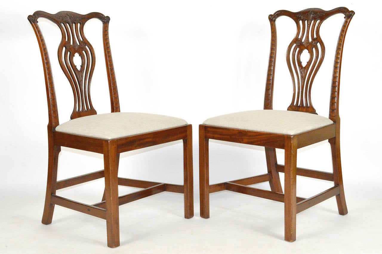A beautiful set of six English Chippendale style caved mahogany side chairs. Each with ox bow crest rail terminating in molded ears surmounting a pierced splat. Seats covered in linen. Resting on square legs, joined by an H-shaped stretcher base,