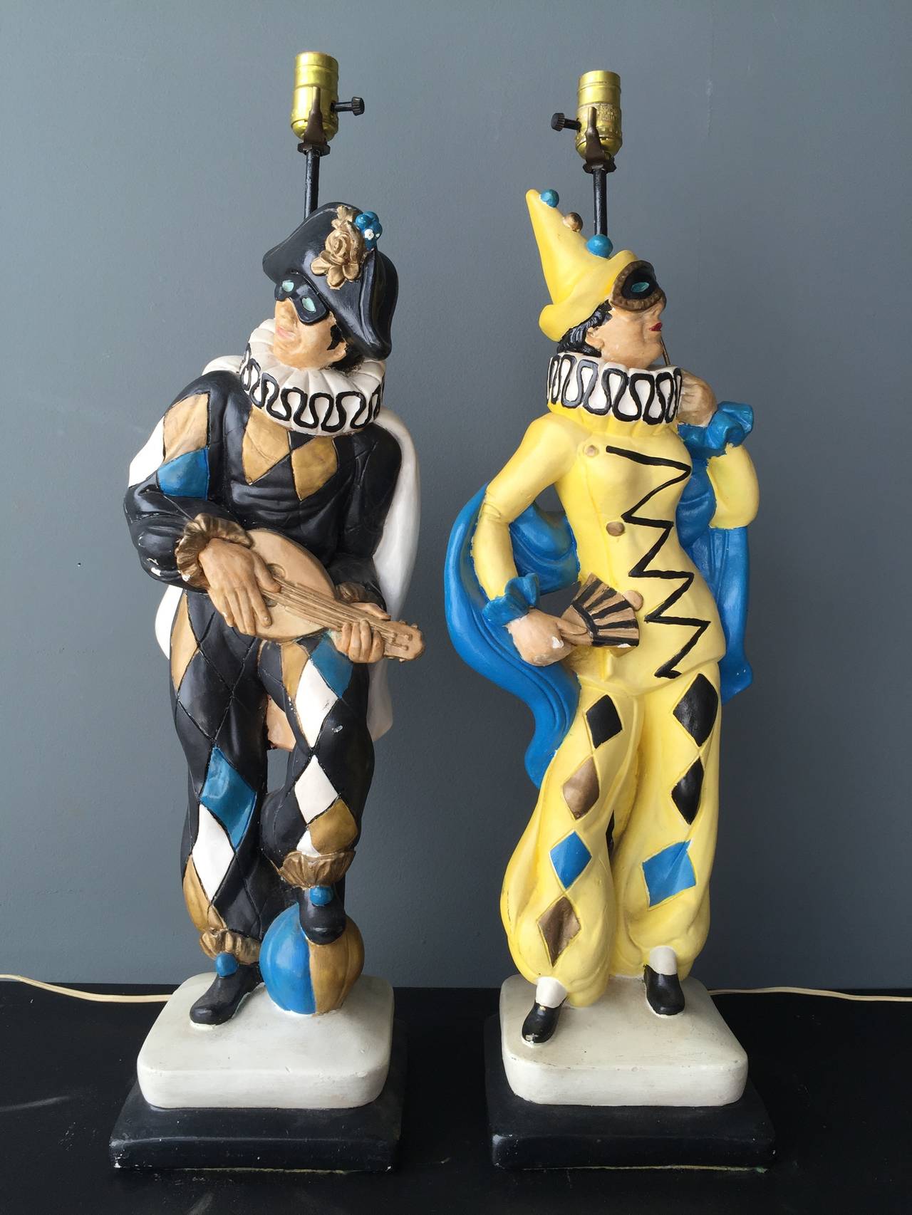 This pair of fanciful jesters in cast plaster with paint decoration is ready to entertain.  With a lute, ball, fan and mask, this pair of table lamps will surely bring a smile to you and your guests.  On solid bases in plaster with the lamp securely
