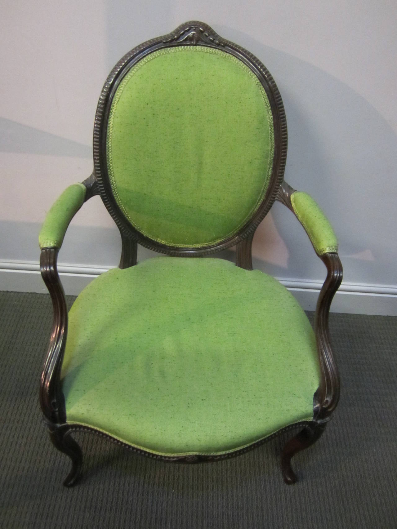 George III mahogany frame open armchair in the French taste, the oval back with a band of fluting and a patera and husk swag cresting, the swept arms over a serpentine seat with fluted apron on slender cabriole legs covered in high quality green