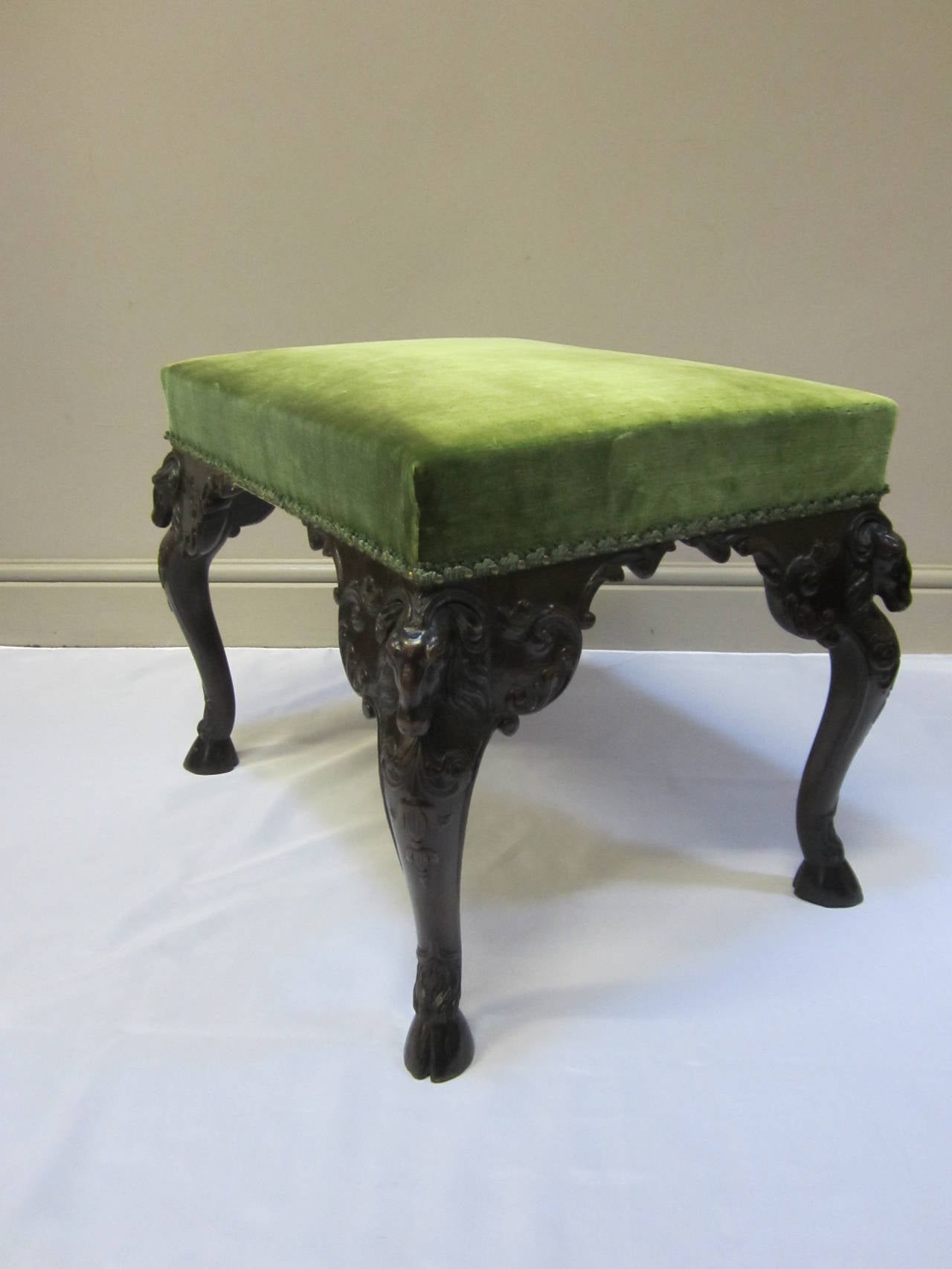 Fine 19th century stool, the deep mahogany frame with intricately carved rams heads on each corner, the cabriole legs sweeping generously concluding in a hoof base, the stool covered in a flecked green silk velvet material with a gimp and stud