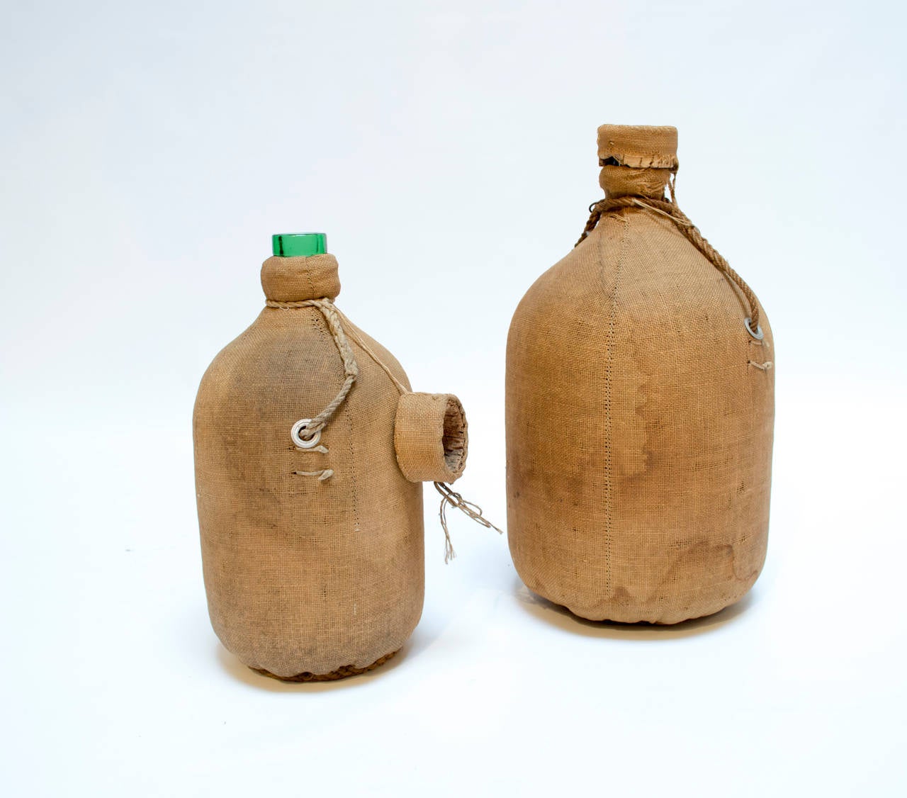 Two antique demijohns wrapped in burlap and horsehair with original cork and burlap caps, circa 1880s. Large bottle measures 20