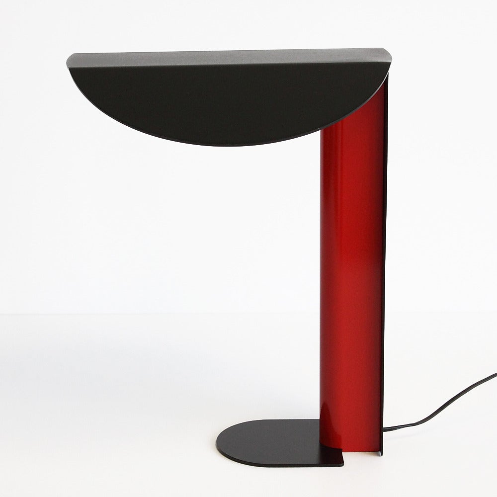 This unique desk lamp features enameled metal construction. The combination of black, red and white enamel make quite the postmodern statement. The black and white angled shade covers an exposed fluorescent tube light bulb. Inline switch. Wired for