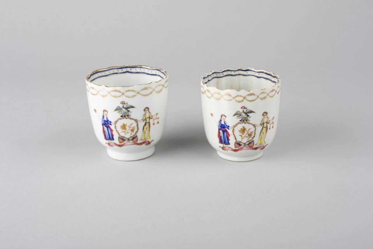 A pair of Chinese export porcelain coffee cups, each with ribbed body and petal shape rim, painted in famille rose enamels with the arms of New York State, one lady holding the scales of justice, with two shields enclosing blue and red
