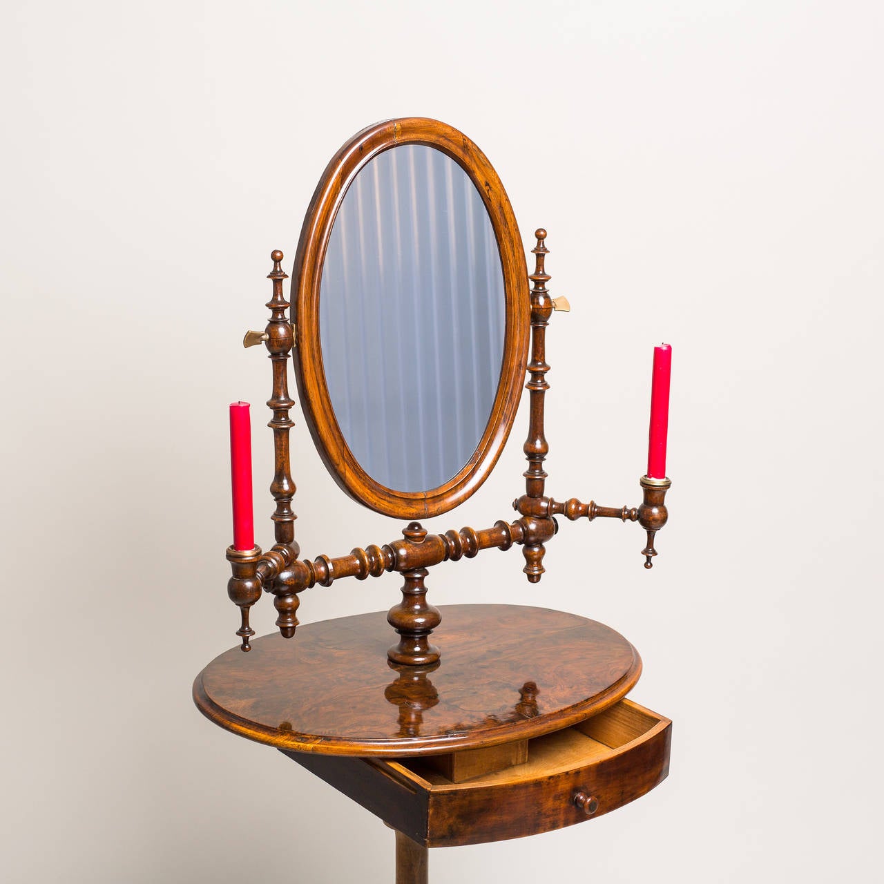 Originating from the period of Louis Philippe, circa 1850, this authentic vanity table features a drawer, mirror, and a pair of candleholders. The intricate spindle-like features, that are found around the oval mirror frame (frame mount and